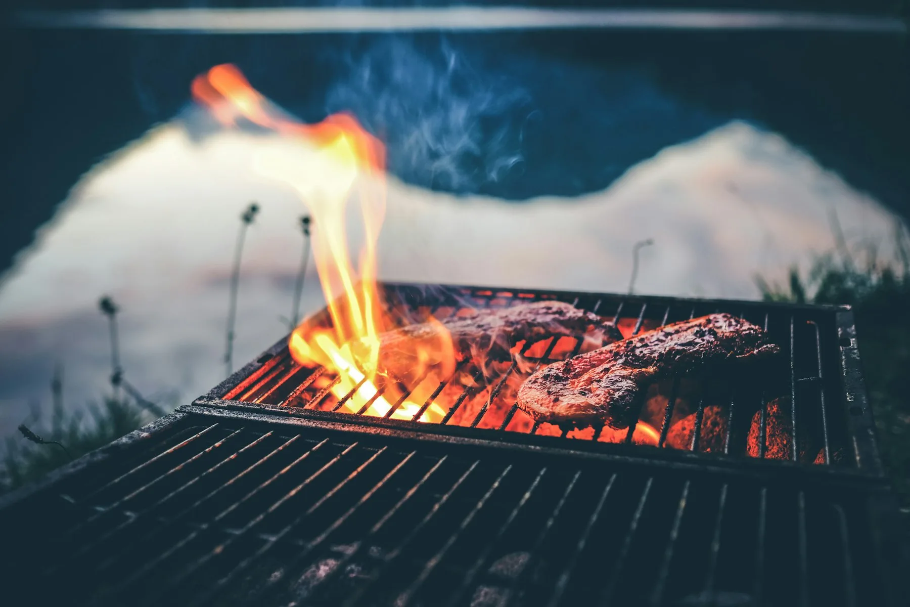 Pièce de bœuf saisie sur un grill au charbon, flammes visibles